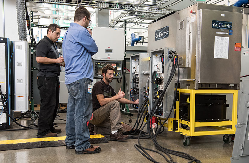Three engineers work on a Go Electric power inverter in a lab. 