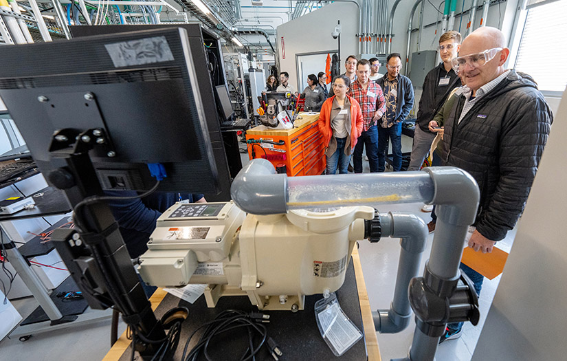 A group of people wearing safety goggles looking at advanced machinery. 