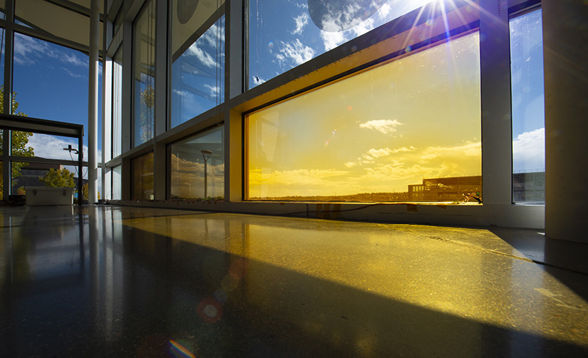 A bay of windows, with an orange photo with the sun shining into a building on the NREL campus.