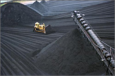 Photo of a yellow bulldozer operating around giant piles of black coal.