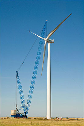 Photo of a large crane maneuvering the rotor and blades onto a wind turbine.