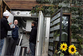 Photo of two young men dressed in black jackets explaining mechanical systems of a solar-powered house to an older man with a beard wearing a light-colored jacket.