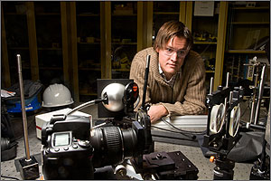 In a photo, a man wearing safety glasses leans over a table where a network of small mirrors and lights has been set up to test the reflective properties of mirror coatings.