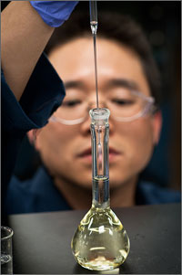 Photo of a man in the background putting a long very thin tube into another container with liquid.