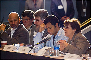 Photo of several men and a woman sitting at a table and speaking into microphones.