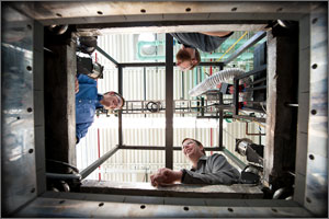 Photo of three men looking into a chamber. Photo is from the bottom of the chamber looking up.