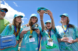 Photo of four girls in matching outfits with medals and trophy.