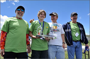 Photo of a four people with a boy holding a racecar and trophy.