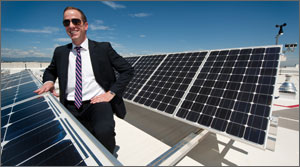 Photo of a man standing on a roof next to a solar panel
