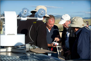 In this photo, most of the men are wearing hats to protect them from the sun. A radiometer is in the foreground, while mesas and mountains are in the background.