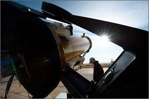 In this photo, an instrument looks almost like the barrel of a gun pointed at the shining sun, while a scientist with his head down walks by, dwarfed by the instrumentation.