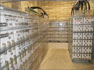 This photo shows a room with brick walls holding stacks of batteries enclosed behind transparent plastic.