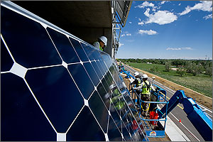 Photo of men on cranes installing photovoltaics on the side of a building.
