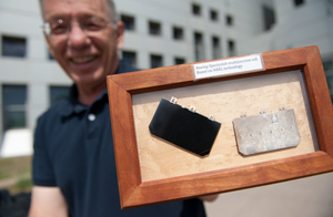 In this photo, a scientist holds at arm's length a wooden frame that contains one black and one white solar cell, each about the size of a deck of cards.
