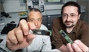 In this photo, two men are extending their hands to show two small electronic devices about the size of sticks of gum. 