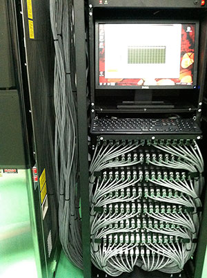 This is a photo of an electronics rack with a computer screen and keyboard above a stack of panels with 128 cables connected to the front of the panels.