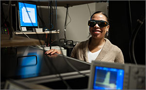 Woman in goggles looks up from a machine in a laboratory.