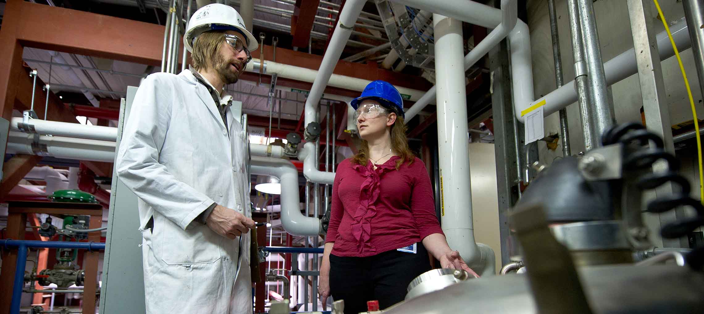 Photo of a man and woman in hard hats inside NREL's Integrated Biorefinery Research Facility. 