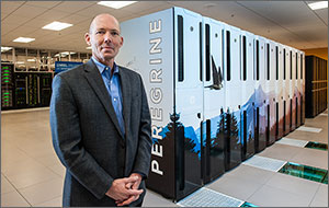 Photo of a man standing in a computer room with a large computer behind him. 