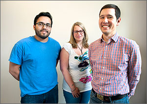 Three smiling people—a woman between two men—stand in an office.