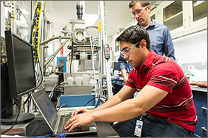 Photo of a man working on laptop computer as another man looks over his shoulder.