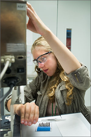 Photo of a woman working with piece of equipment in science lab.