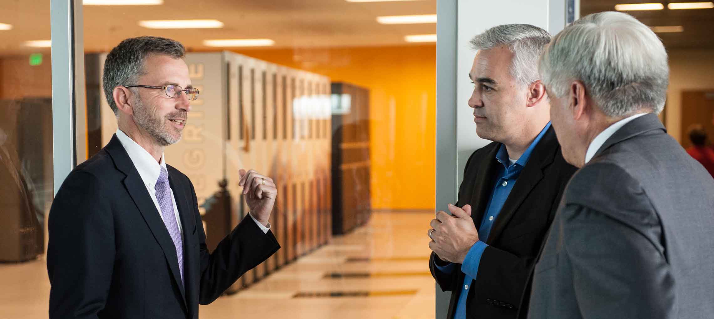 This photo shows three men in suits standing in front of a data center.