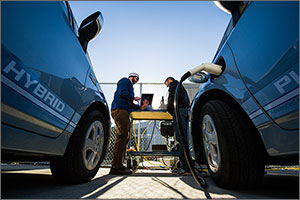 Photo of two men stranding at a computer stationed between two vehicles.
