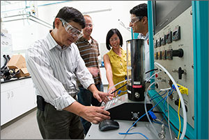 Photo of three men and one woman looking at instruments in a laboratory. 