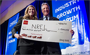 Photo of a woman and a man smiling and holding an oversized check addressed to NREL for $10 million.