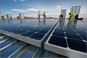 Photo of men in safety gear working to install PV modules on a rooftop.