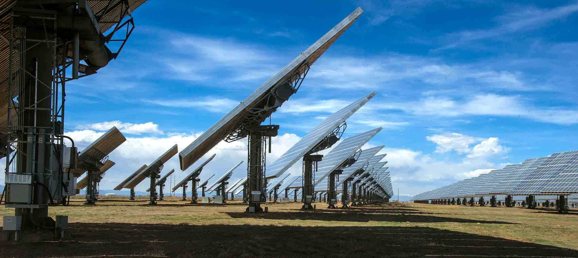 This photo shows numerous solar modules tilted toward the sun with a blue sky interspersed with white clouds in the background.