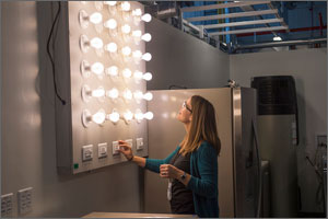 Photo of a woman in a laboratory standing in front of a bank of lightbulbs, adjusting the switches.