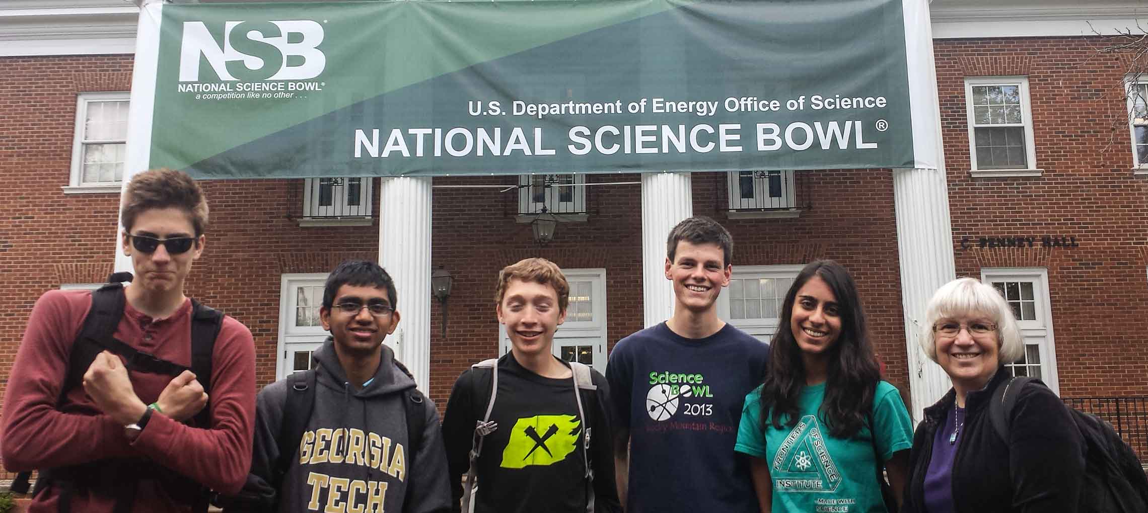 Photo shows five students and their coach standing beneath a banner for the National Science Bowl.