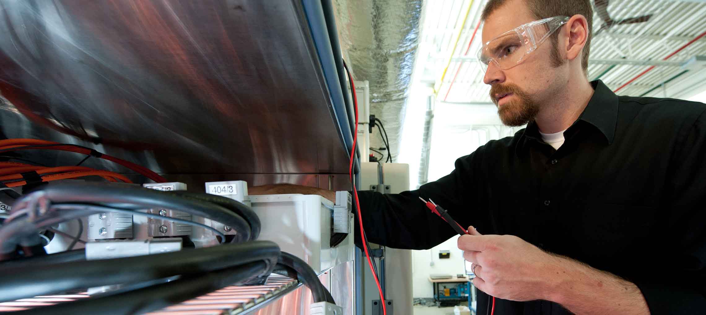 Photo of a man in a lab, holding cables.