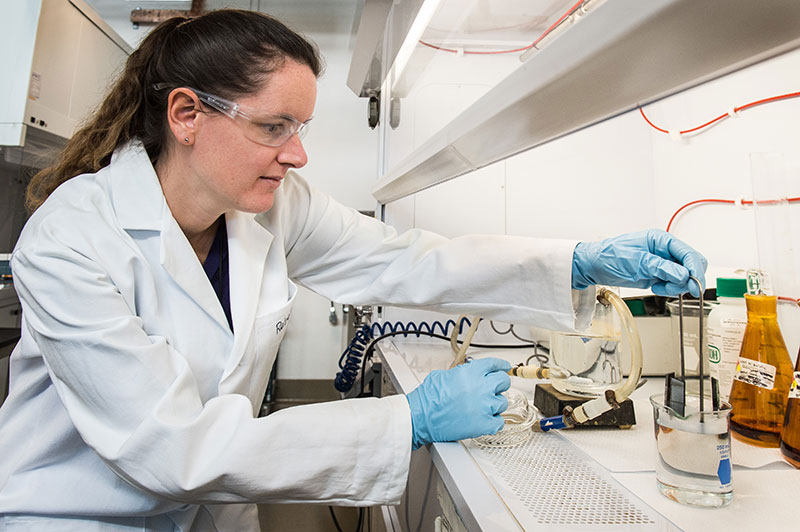 A woman in a lab coat works with instruments in a laboratory.
