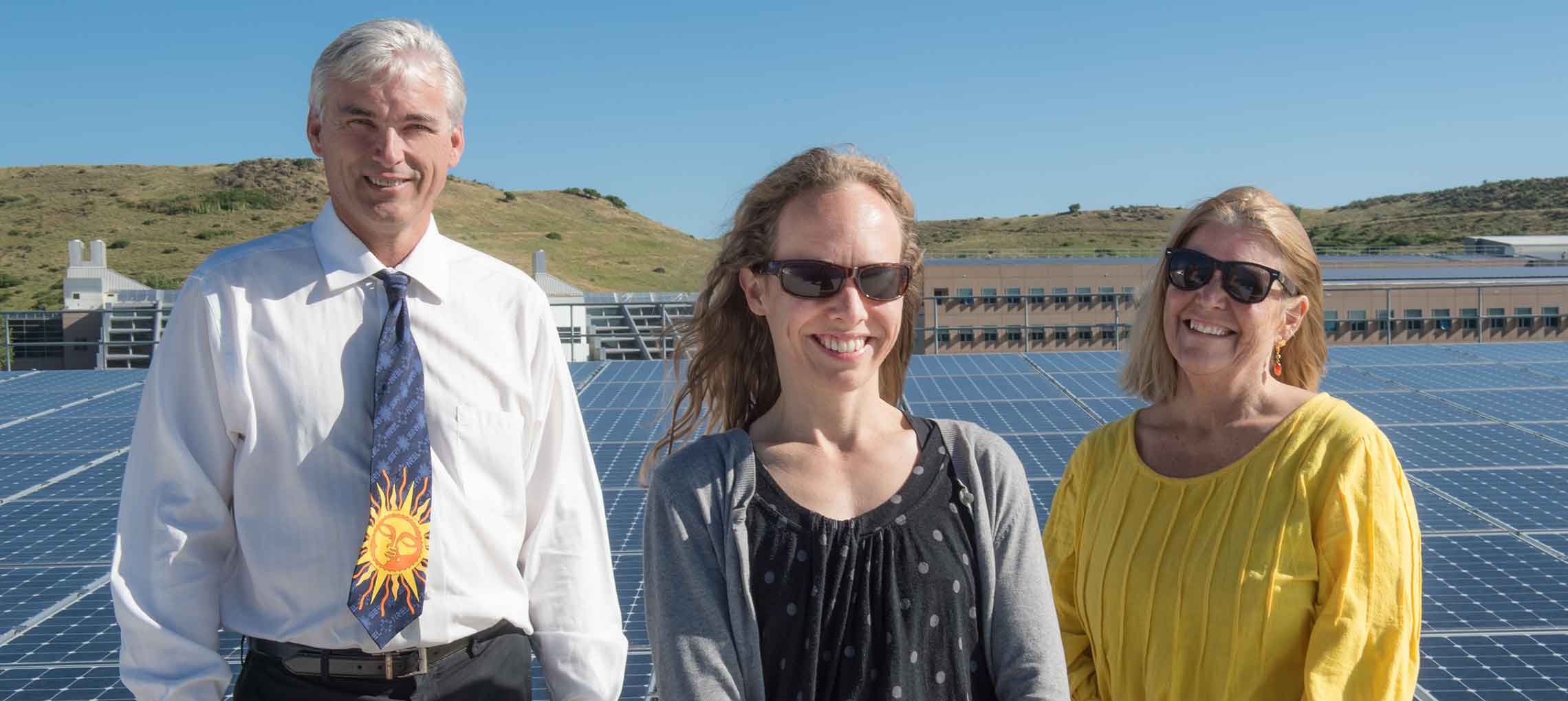 Three people stand in front of solar panels on top of the NREL parking garage.