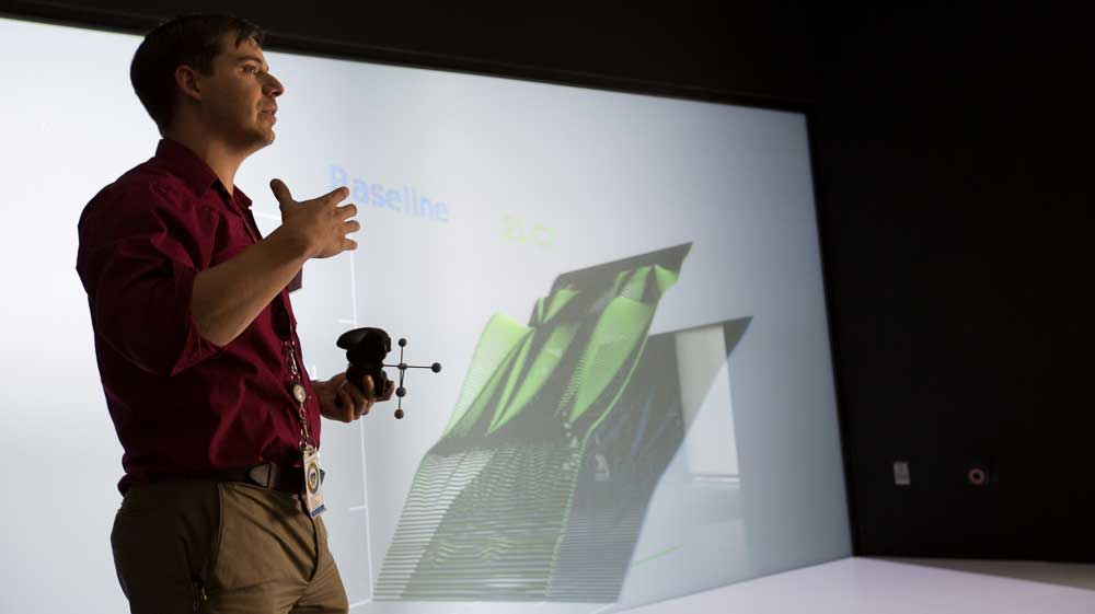 Photo of a man standing in front of a 3-D screen.