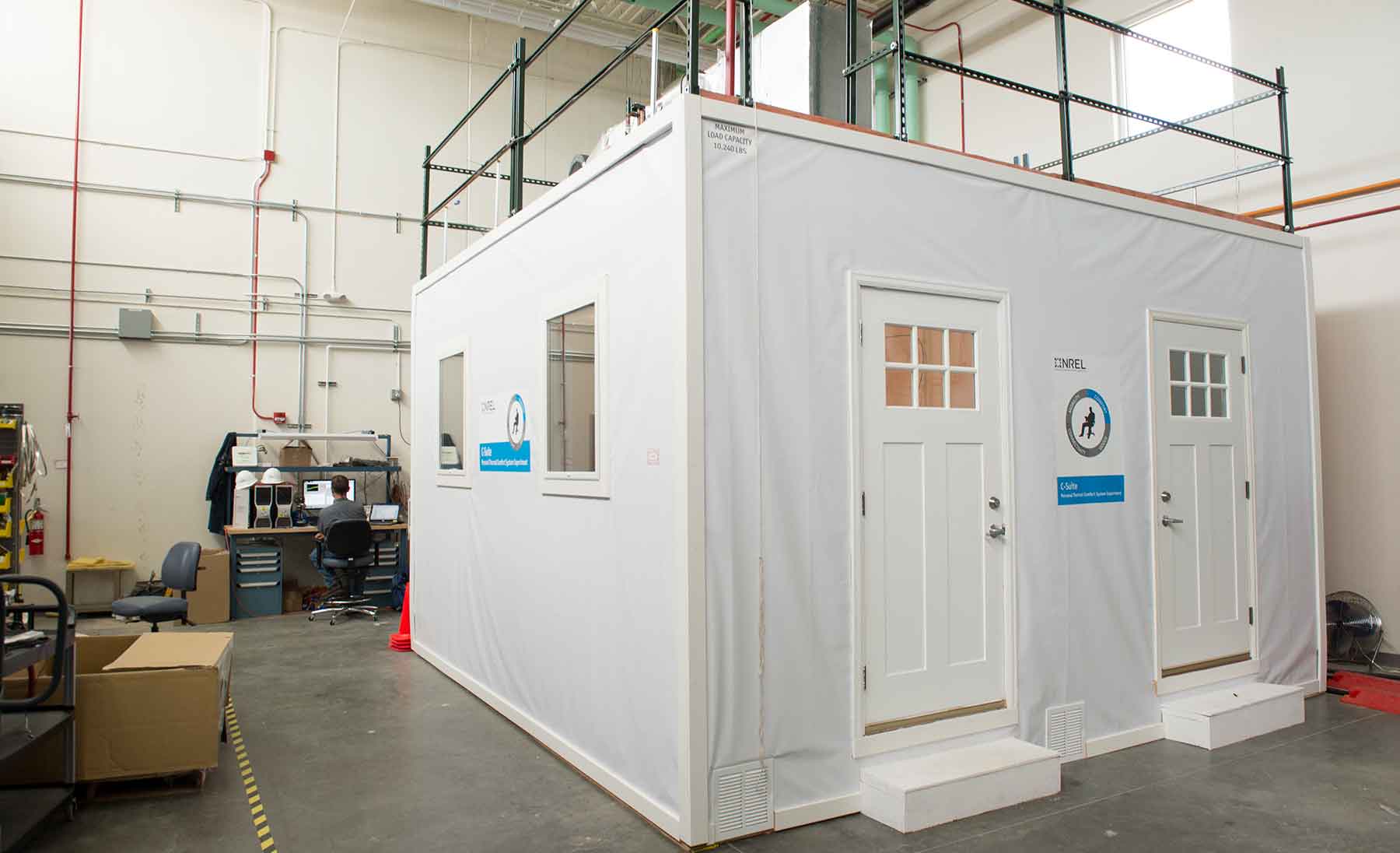 Photo shows the Comfort Suite structure, a white room with two doors and windows in a laboratory facility.