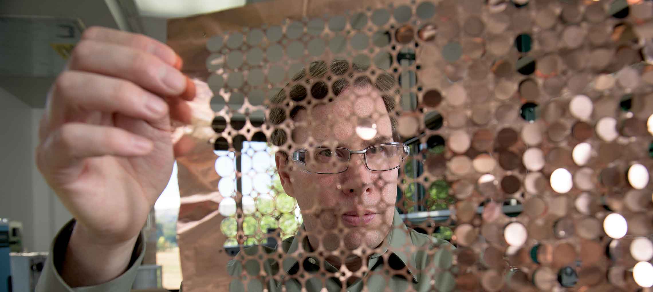 A man holds a sheet of copper discs.