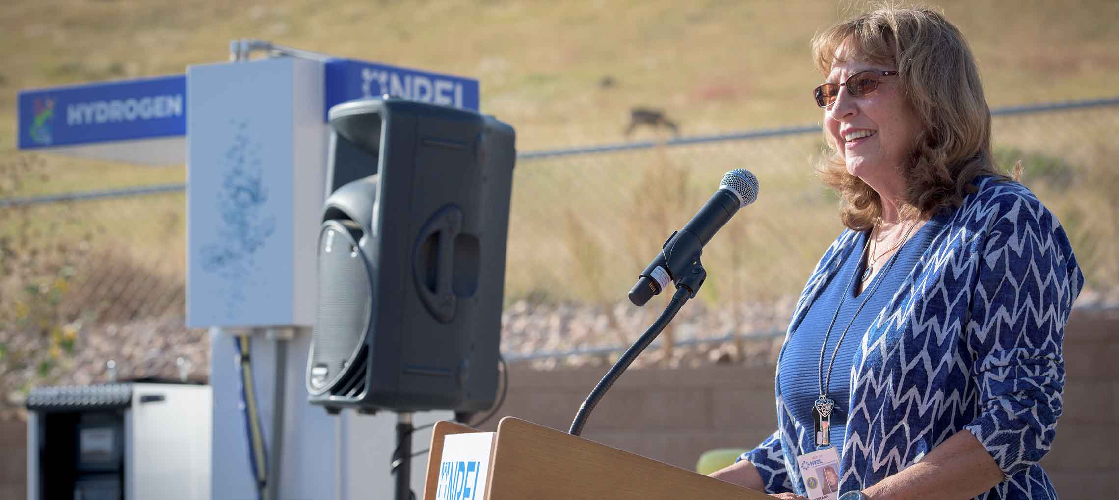 Woman stands outside in front of a podium next to a hydrogen fueling pump.