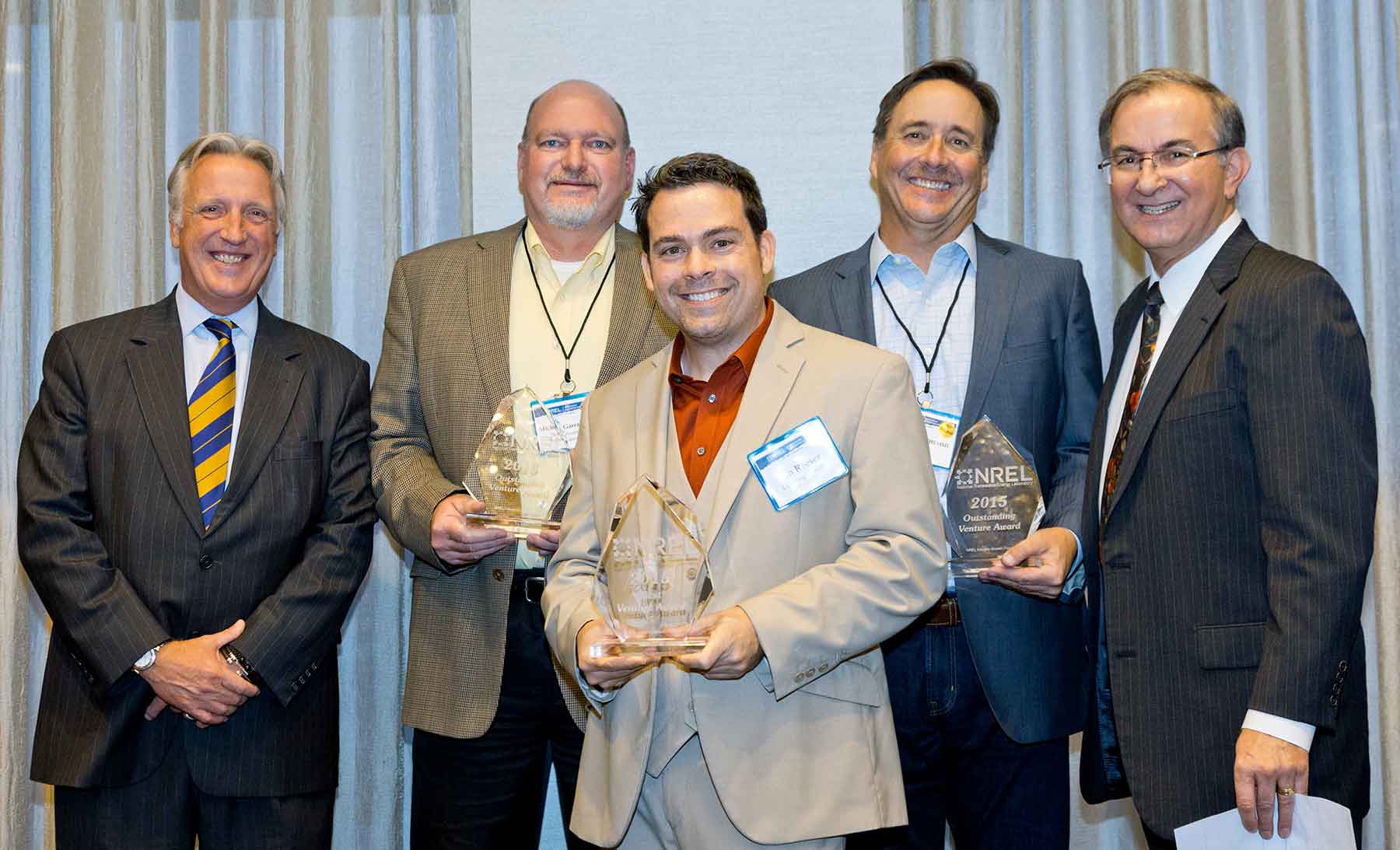 Five men share the stage at the conclusion of the IGF. Three hold glass trophies.