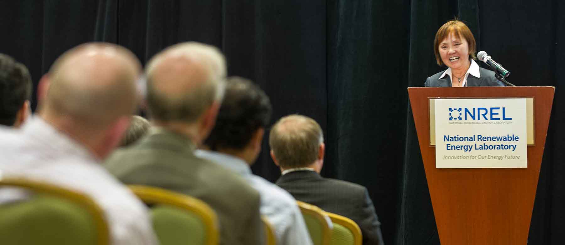 A woman at a podium addresses an audience.