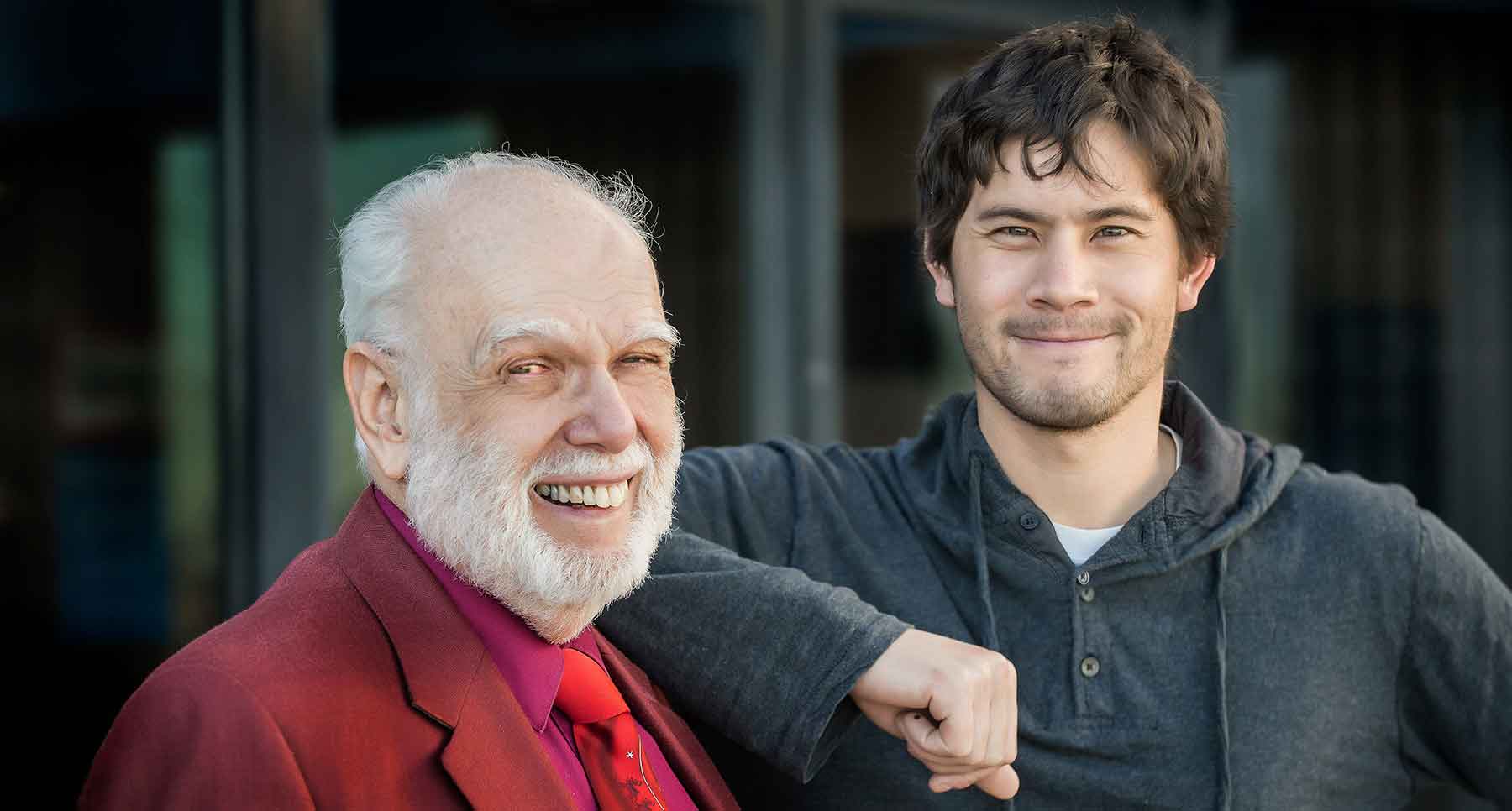 Two smiling men stand shoulder to shoulder.