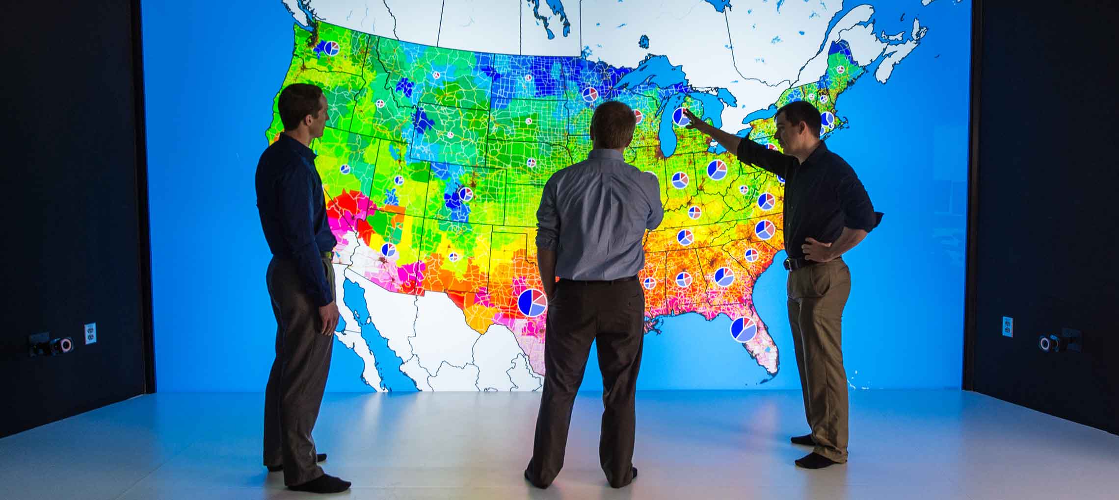 NREL researchers look at colored map of the United States in 3D visualization room.