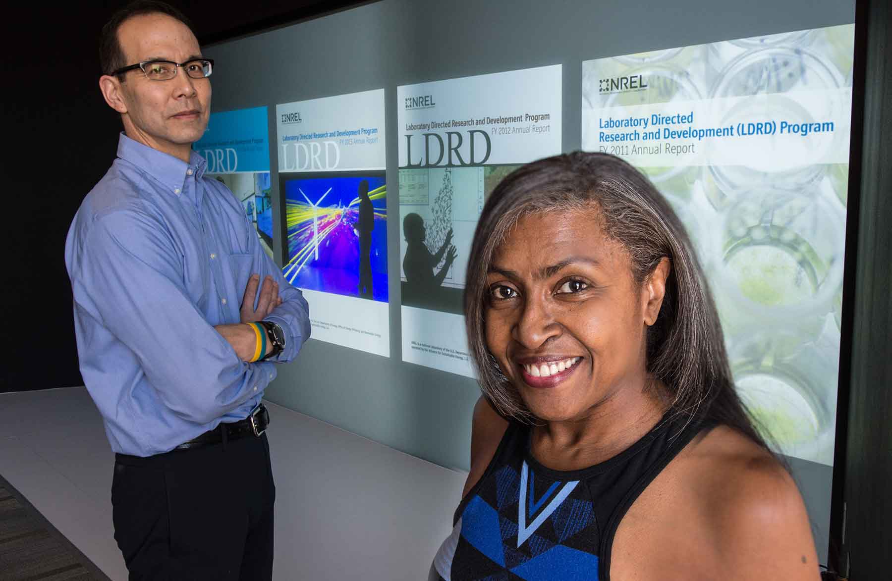 Two people stand in front of a screen displaying reports about NREL's LDRD program.