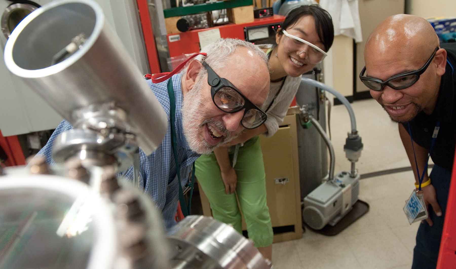 Two men and a woman in goggles look at a piece of lab equipment.