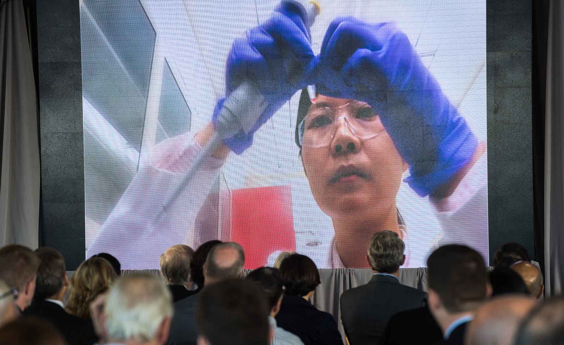 Image shows the audience watching a video of a female scientist at work.