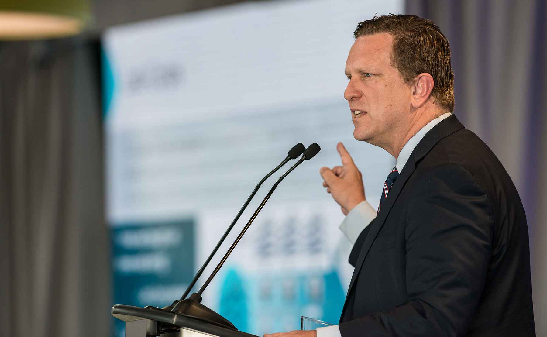 A man stands in front of microphones at a podium.