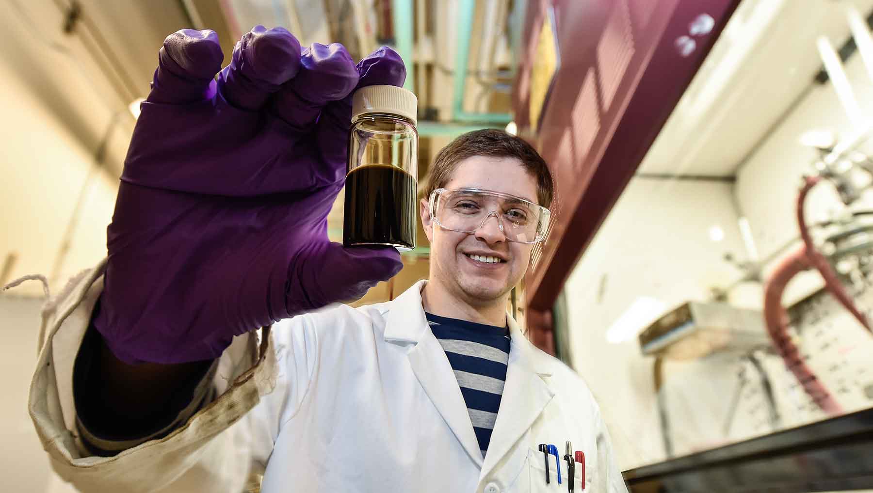 A man in a laboratory displays a solution in a small enclosed glass tube.